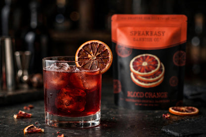 Dried blood orange wheel on a cocktail glass rim, Speakeasy Garnishes pouch in background