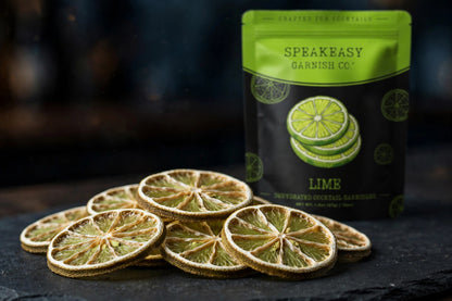 Dried lime wheels fanned on dark slate with Speakeasy Garnishes pouch behind
