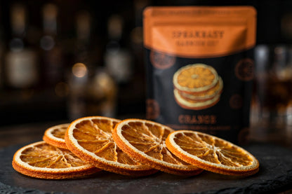 Dried orange wheels fanned on dark slate with Speakeasy Garnishes pouch behind